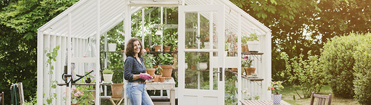 Frau vor einem Gewächshaus im Garten